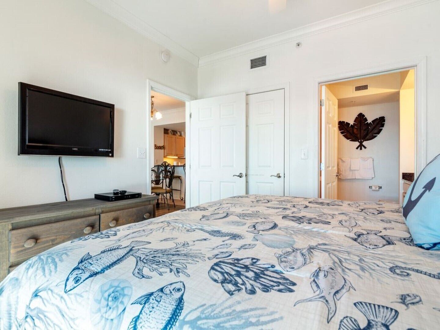 A bedroom with a bed featuring a fish pattern, a television on the wall, and white doors leading to other rooms.