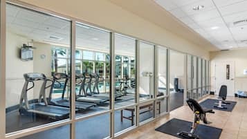 Een fitnessruimte met loopbanden, hometrainers en een zwembadgedeelte, zichtbaar door glazen wanden.