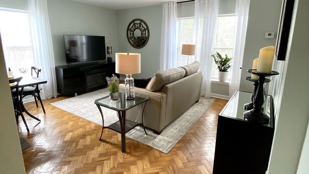 A living room with a herringbone wooden floor, a sofa, a TV, and a lamp. - The Paris Loft in the heart of downtown (Safety Harbor)