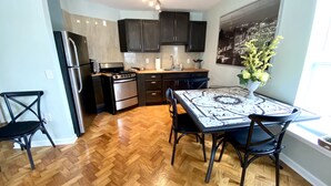 A modern kitchen with dark cabinets, a stainless steel refrigerator, a gas stove, and a dining area with a patterned table and chairs. - The Paris Loft in the heart of downtown (Safety Harbor)