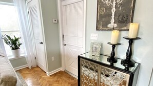A hallway with a herringbone wooden floor, a beige sofa, a glass cabinet with candles, and a decorative wall piece. - The Paris Loft in the heart of downtown (Safety Harbor)