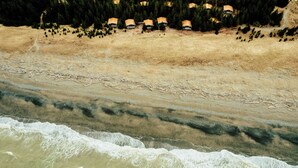 Zona costera con playa, olas y una hilera de cabañas.
