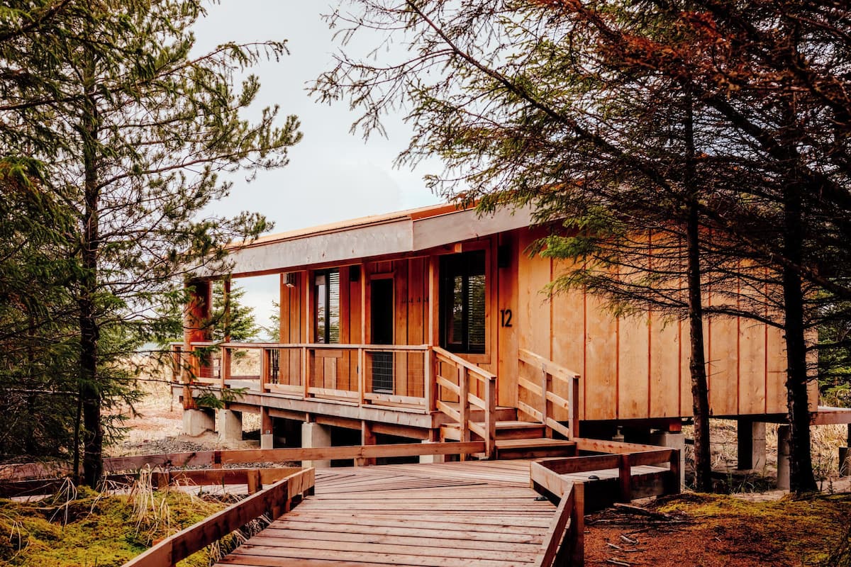 A wooden cabin with a deck, surrounded by trees.