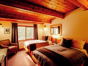 A room with a wooden ceiling, a bed with a headboard, a desk, a chair, a window with curtains, and a wall-mounted mirror.