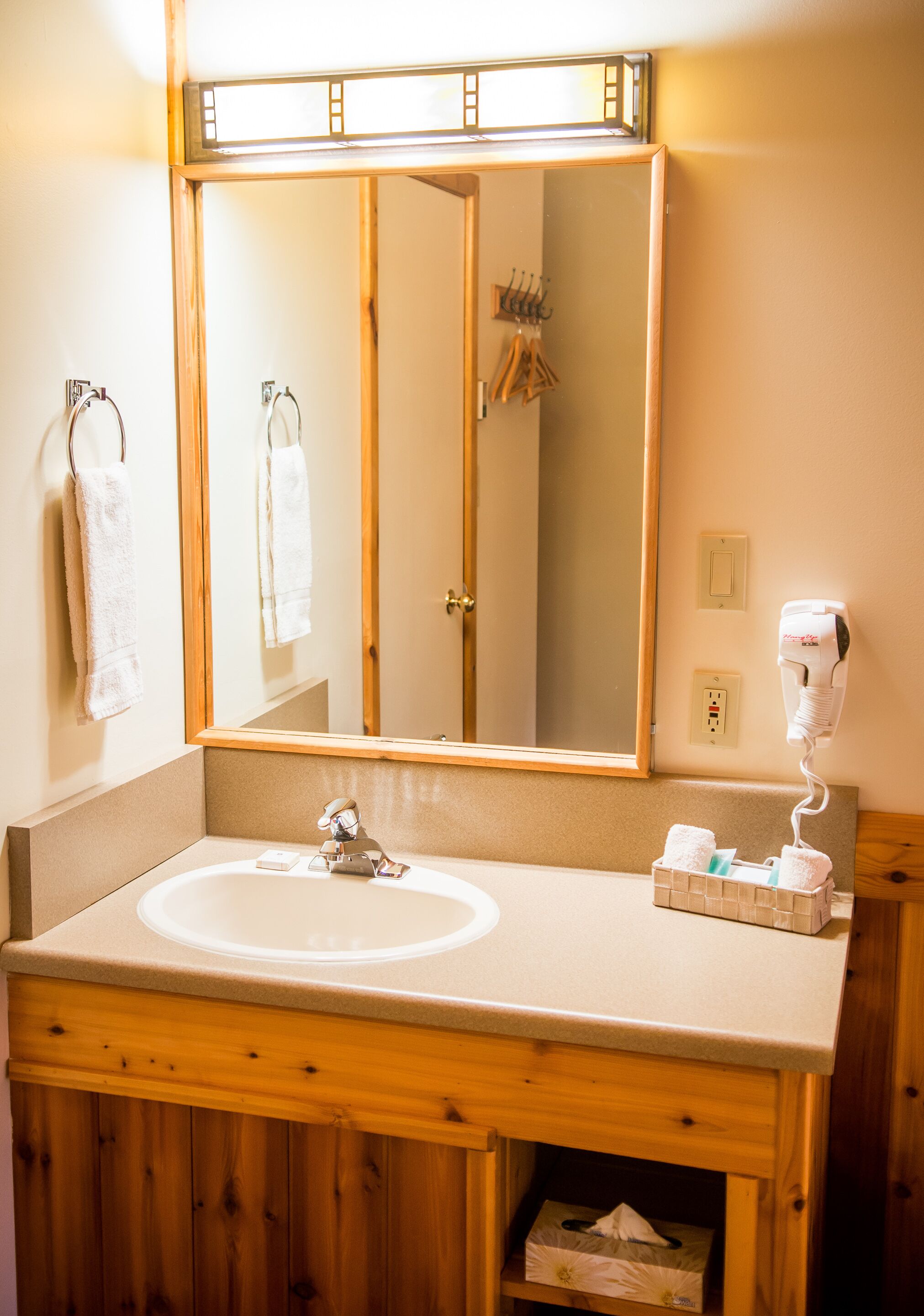 A bathroom with a wooden vanity, a large mirror, a hairdryer, and a towel rack.