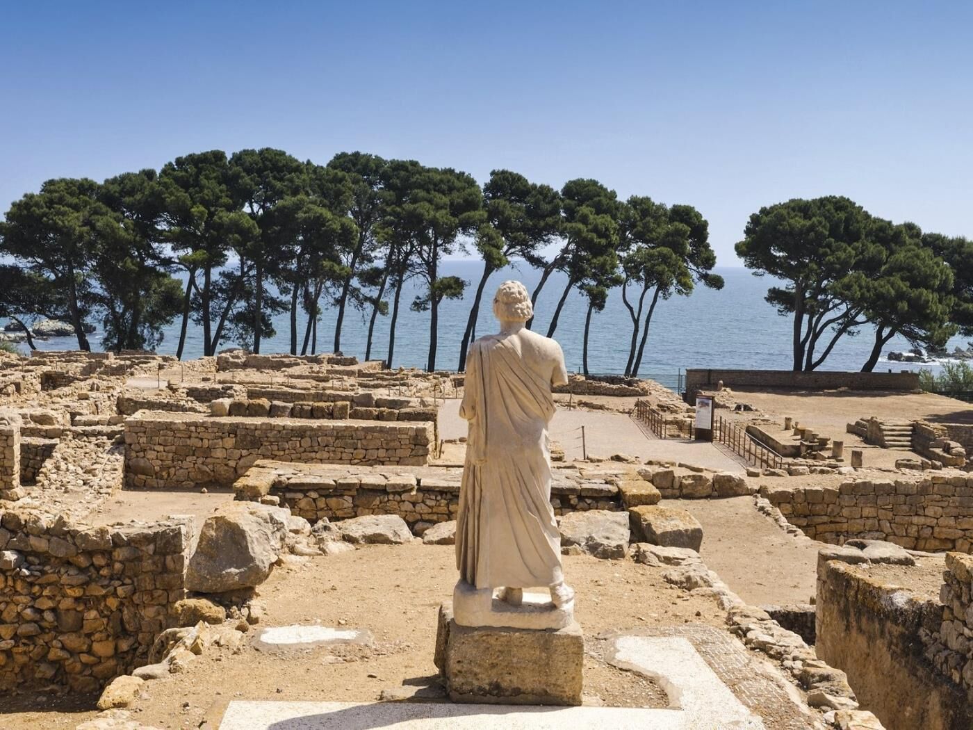 Een oude archeologische plek met ruïnes en een standbeeld op de voorgrond.