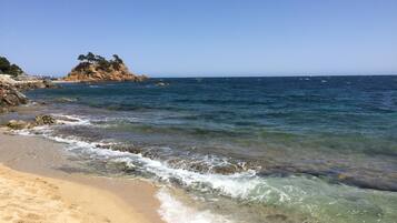 Una playa con aguas cristalinas, orilla arenosa y un promontorio rocoso con árboles.