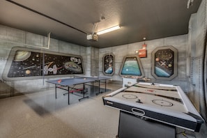 Experience the cosmic vibe in this futuristic room, featuring a ping pong table, foosball table, and stunning space-themed artwork.