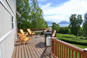 Une terrasse en bois avec des meubles d’extérieur, un barbecue et une bouteille de propane.