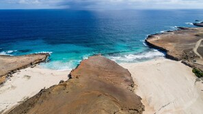 Paisagem costeira com uma praia de areia e falésias rochosas sobre o oceano.