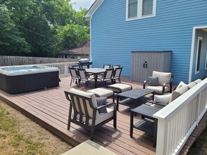 Une terrasse avec un jacuzzi, du mobilier d’extérieur et une maison bleue en arrière-plan.