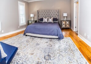 Une chambre à coucher avec un grand lit, deux tables de chevet, une commode, une chaise bleue et un tapis à motifs.