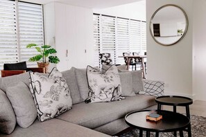 Uma sala de estar moderna com um sofá cinza, almofadas estampadas, um espelho redondo e uma pequena mesa redonda com um livro.