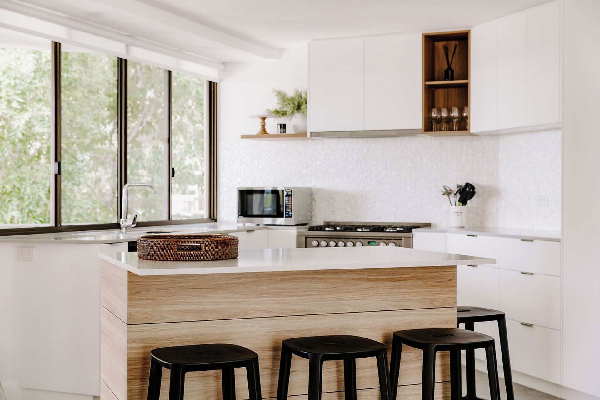 Una cucina moderna con isola centrale, sgabelli da bar, microonde e forno integrato.
