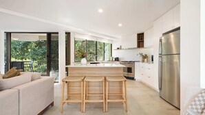 A modern kitchen with a central island, stainless steel appliances, and a view of greenery outside.