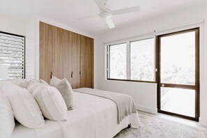 A bedroom with a bed, a ceiling fan, a large window, and a sliding door.