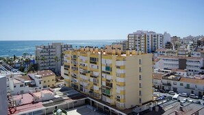 A coastal cityscape with a prominent yellow building featuring balconies and a clear view of the sea.