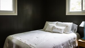 A bedroom with a bed, two windows, and a nightstand with a lamp.
