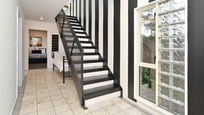 Un escalier moderne aux rayures noires et blanches, menant à une chambre à coucher équipée d’un lit et d’une grande fenêtre.