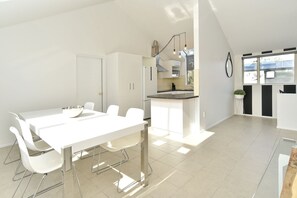 A modern kitchen with white cabinetry, a dining area with a white table and chairs, and a large window providing natural light. - Moa Place - Christchurch Holiday Homes (Christchurch)