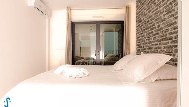 A hotel room with a bed, a window with curtains, a brick wall, and an air conditioning unit. - Nice apartment for 4 with parking, near Cité du Vin (Bordeaux)