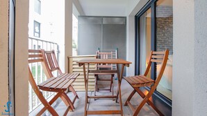A balcony with a wooden table and four chairs, a window with a view of buildings, and a door with a glass panel. - Nice apartment for 4 with parking, near Cité du Vin (Bordeaux)