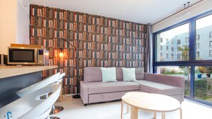 A modern living room with a sectional sofa, a small round table, a microwave, and a bookshelf. - Nice apartment for 4 with parking, near Cité du Vin (Bordeaux)