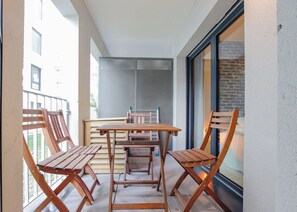 A balcony with a wooden table and four chairs, a window with a view of buildings, and a door with a glass panel. - Nice apartment for 4 with parking, near Cité du Vin (Bordeaux)