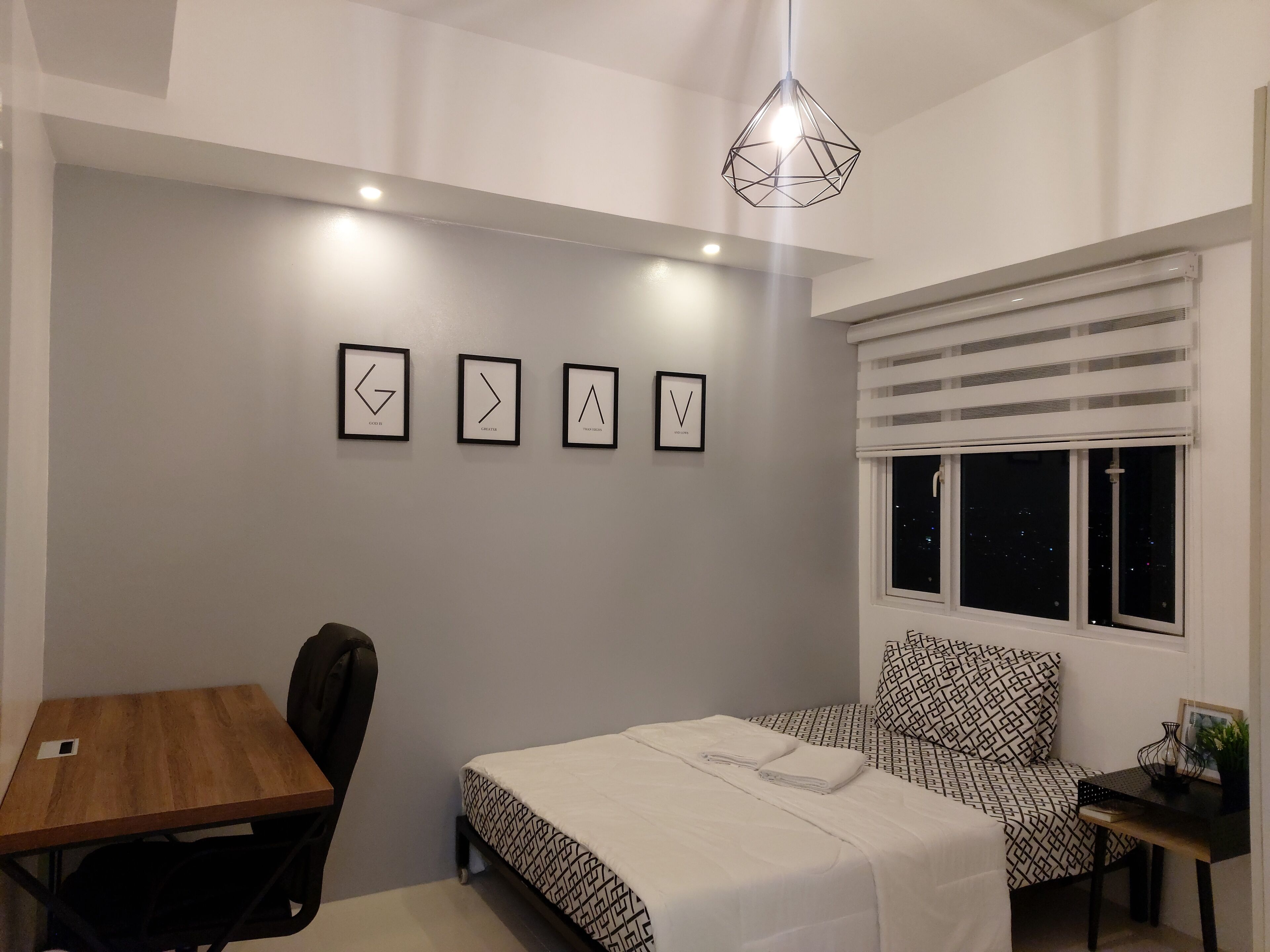 Un dormitorio con cama, escritorio, silla, ventana con persianas y tres cuadros en la pared.