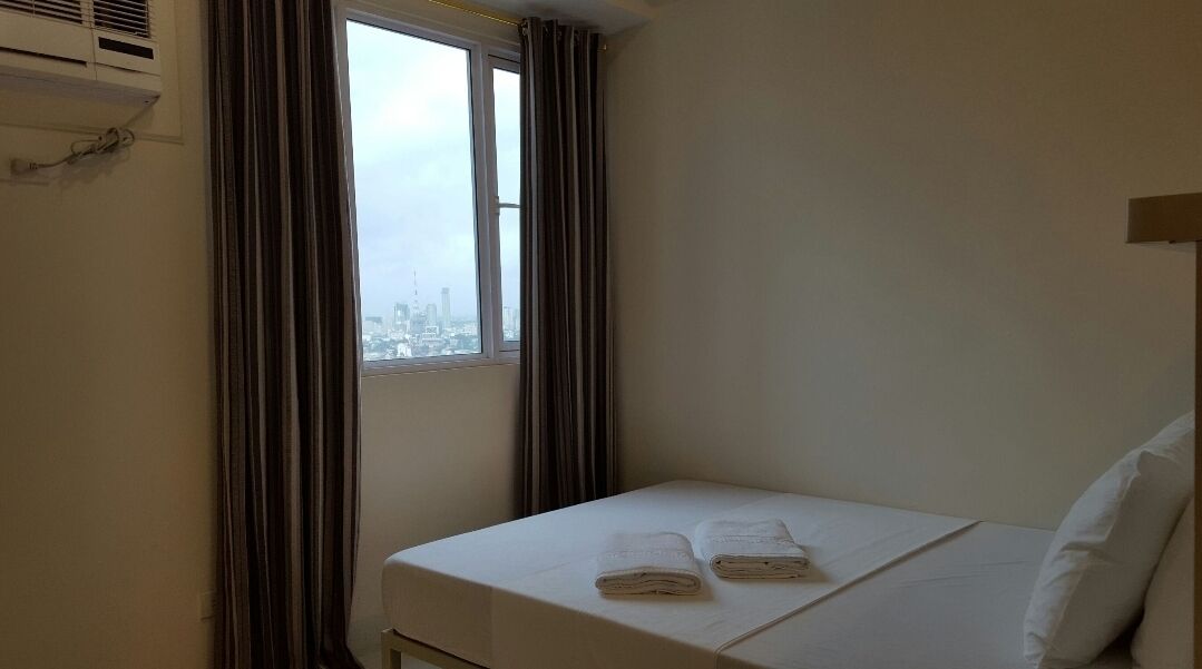 A hotel room with a bed, a window with curtains, and a city view.