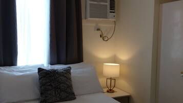 Een hotelkamer met een bed, een bedlamp, een airconditioningsysteem en een raam met gordijnen.