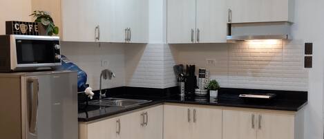 A modern kitchen with white cabinets, a stainless steel refrigerator, a microwave, and a sink.