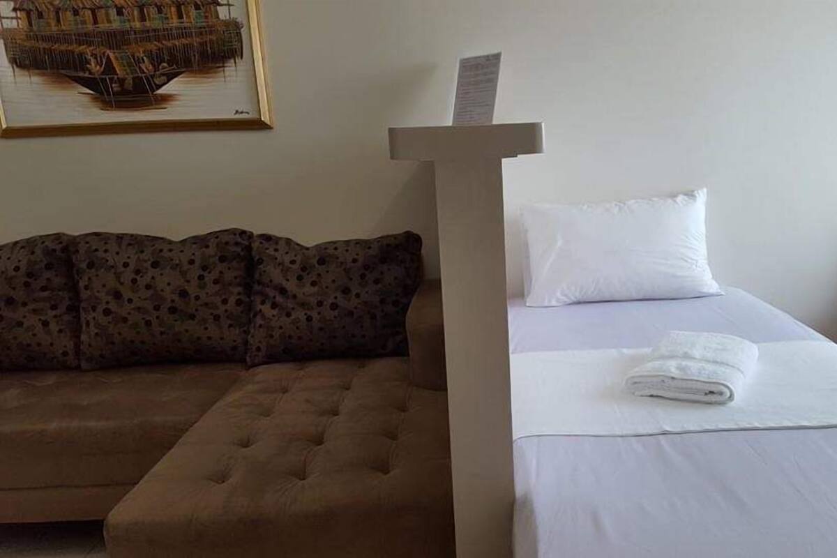 Une chambre d’hôtel avec un canapé marron, un lit avec du linge de lit blanc et un tableau au mur.