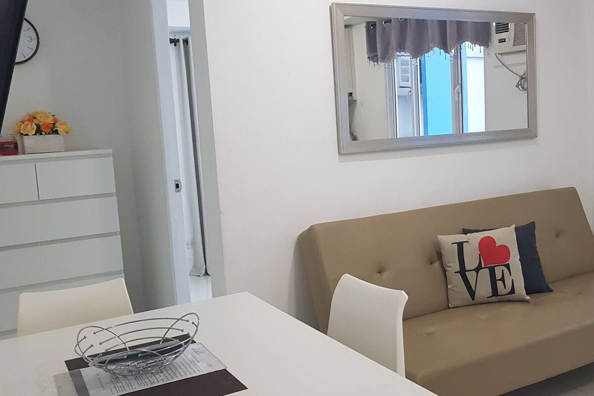 Un salon avec un canapé beige, une table à manger blanche et un miroir au mur.