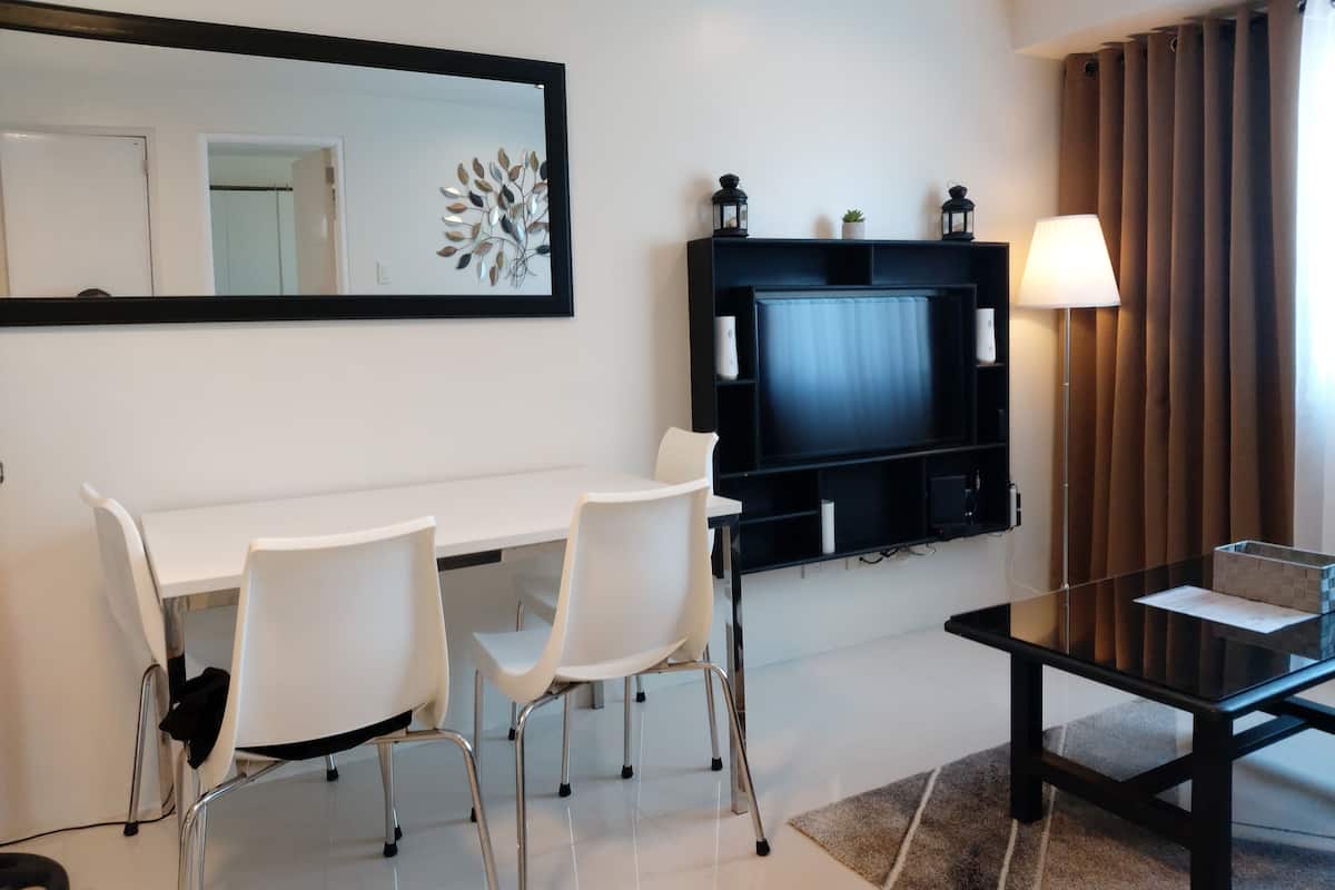 Une chambre d’hôtel moderne équipée d’un téléviseur à écran plat, de chaises blanches, d’une table en verre et d’un grand miroir.