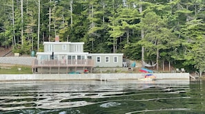A two-story house with a dock extending into a lake, surrounded by trees.