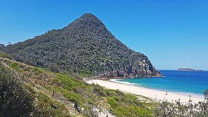 Paisatge costaner amb un turó destacat, una platja sorrenca i l'oceà.