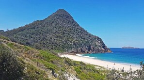 Un paysage côtier caractérisé par une colline imposante, une plage de sable et l’océan.