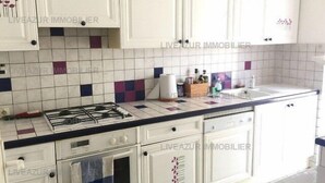 Cucina con mobili bianchi, zoccolo a piastrelle, piano cottura a gas e lavello.