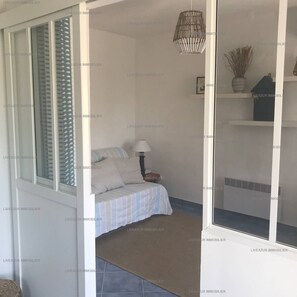 A bedroom with a bed, a nightstand, a lamp, a hanging light fixture, and a window with blinds.