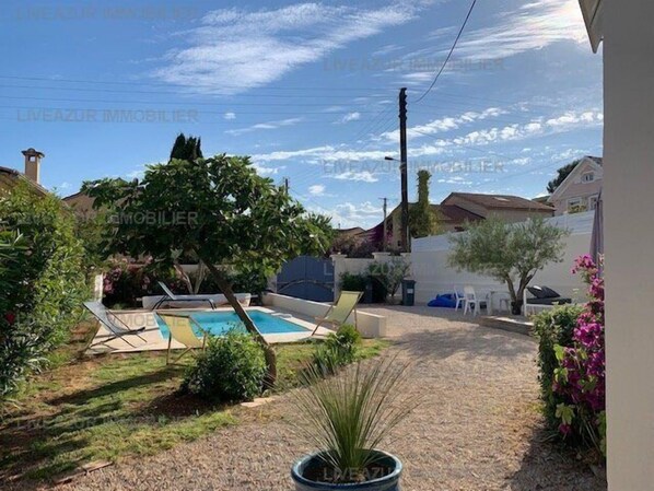 A backyard with a swimming pool, a small garden, and a white wall.