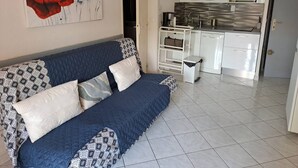 A living room with a sofa, a painting, and a kitchen area with white cabinets and appliances.