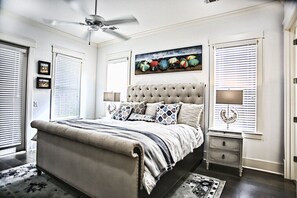 A bedroom with a tufted headboard, a bed with a striped bedspread, two bedside tables with lamps, and a ceiling fan.