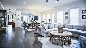 A spacious living room with a large sofa, a round coffee table, and a ceiling fan. - 1-14 Guest: Pool/Fire Pit/Bikes/Putting Green/Polaris Ranger Included Aug-Dec 25 (St Simons)