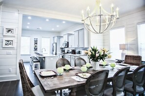 A modern kitchen with white cabinets, a dining area with a wooden table, and a chandelier. - 1-14 Guest: Pool/Fire Pit/Bikes/Putting Green/Polaris Ranger Included Aug-Dec 25 (St Simons)