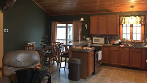 A cozy cabin interior with a dining area, kitchen, and a mounted deer head. - Adirondack Experience (Old Forge)