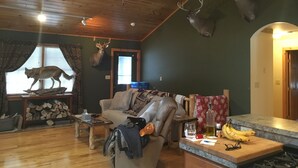 A cozy living room with a wooden ceiling, a fireplace, a mounted deer head, and a couch. - Adirondack Experience (Old Forge)