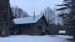 A wooden cabin with a sloped roof, a chimney, and a small porch with steps leading to the door. - Adirondack Experience (Old Forge)