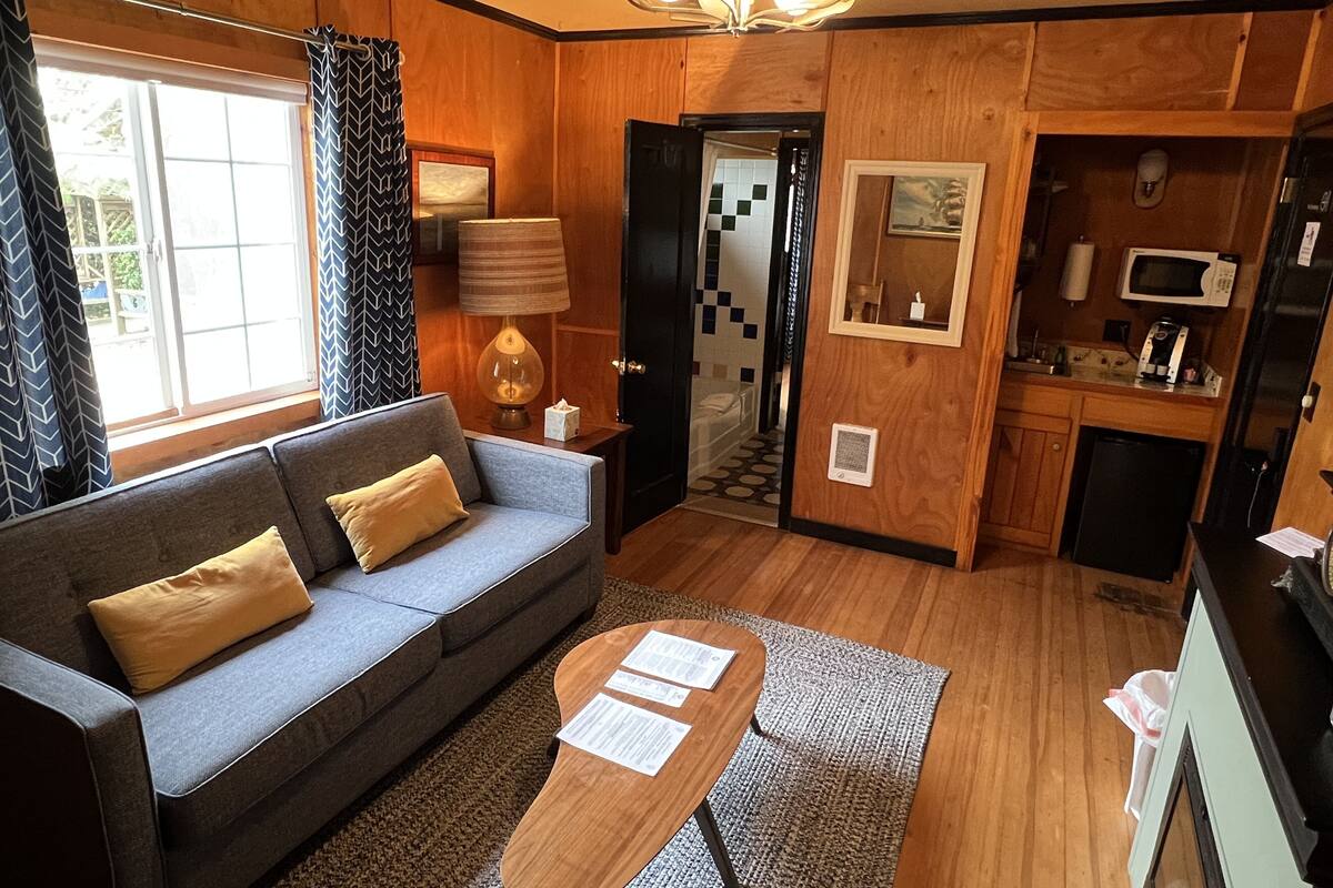 A compact living space with a sofa, a small coffee table, a kitchen area with a microwave and refrigerator, and a door leading to a bathroom with a tiled shower.