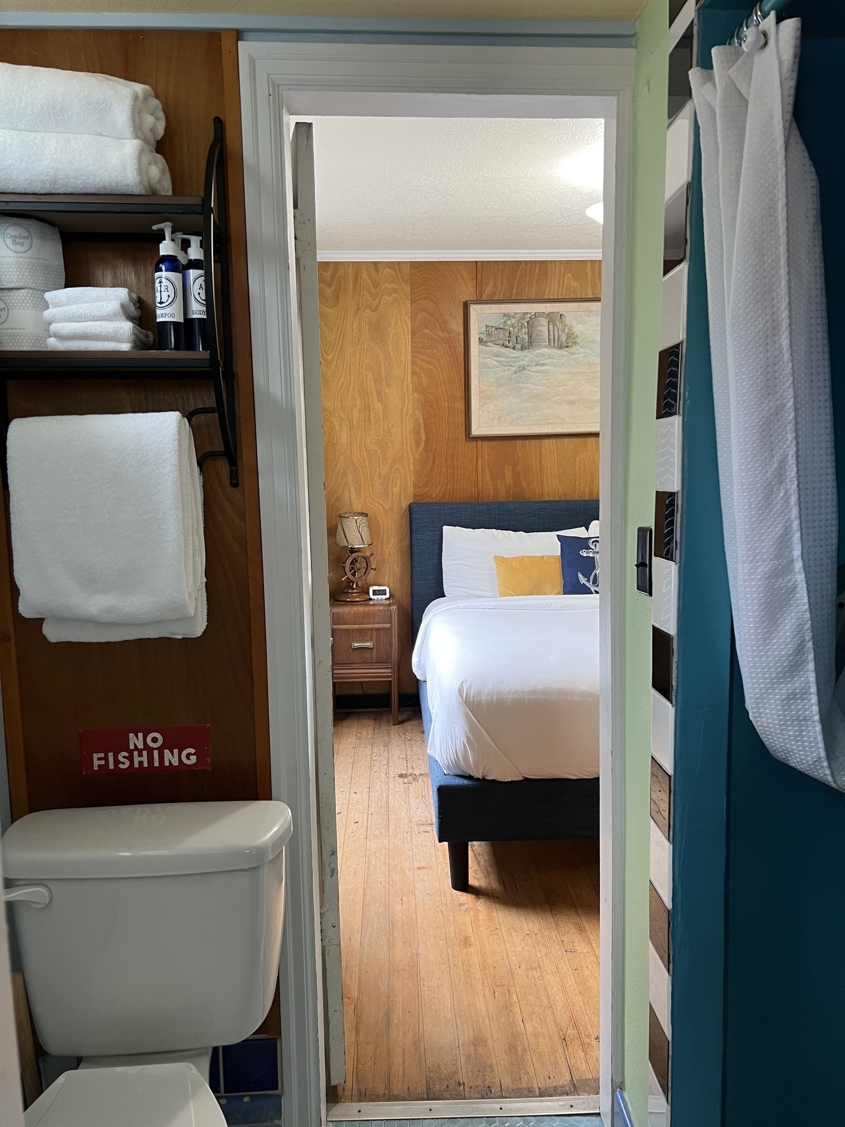 Une salle de bain d’hôtel avec des toilettes, une étagère avec des serviettes et des articles de toilette, et un panneau indiquant « PÊCHE INTERDITE ».